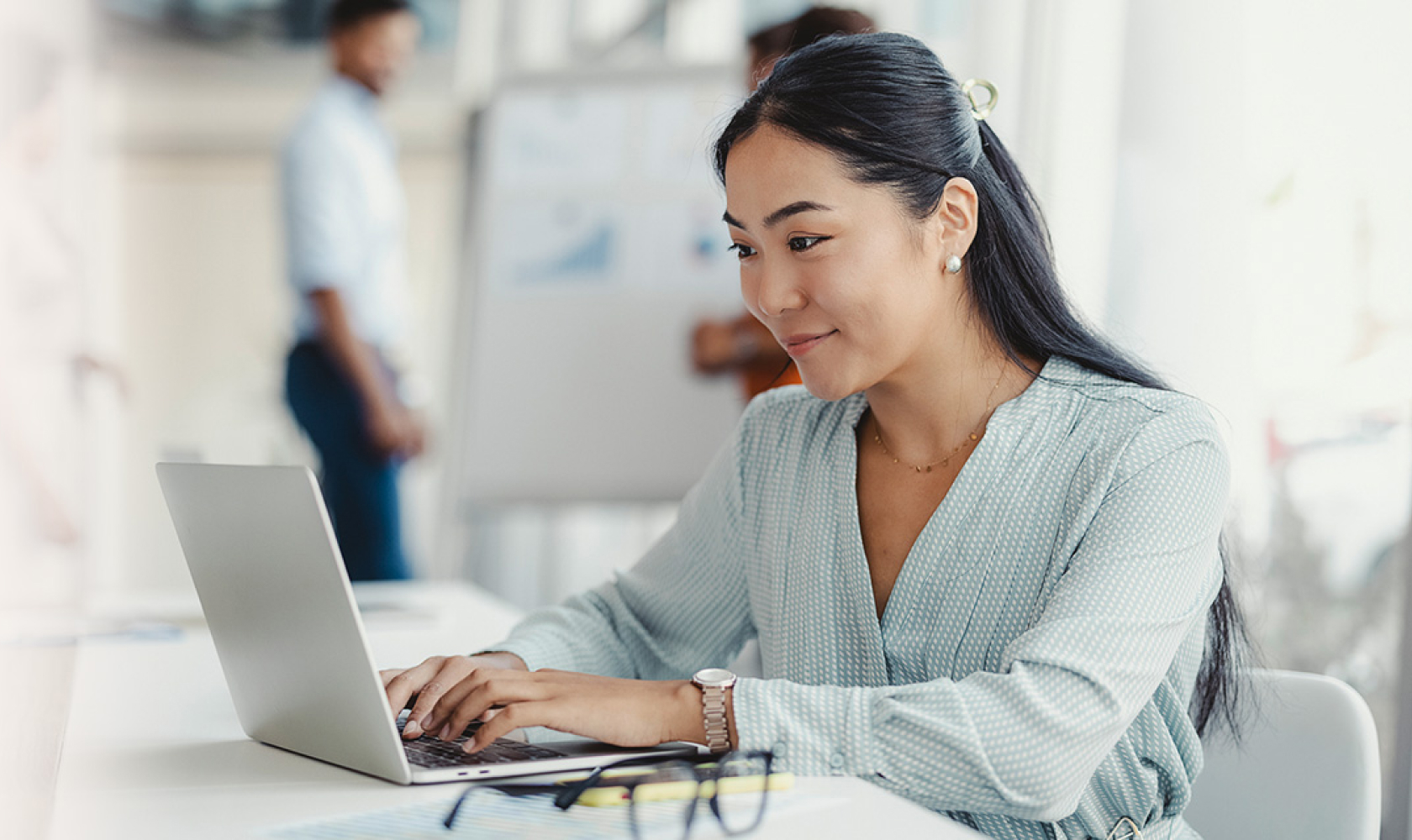 A woman sitting at a worktable uses a laptop.