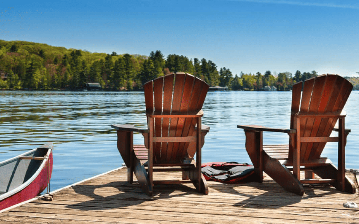 Deux chaises en bois reposent sur un quai au bord d&rsquo;un lac, &agrave; c&ocirc;t&eacute; d&rsquo;un canot.