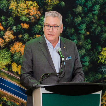 Canada Post President and CEO, Doug Ettinger stands at a podium speaking.