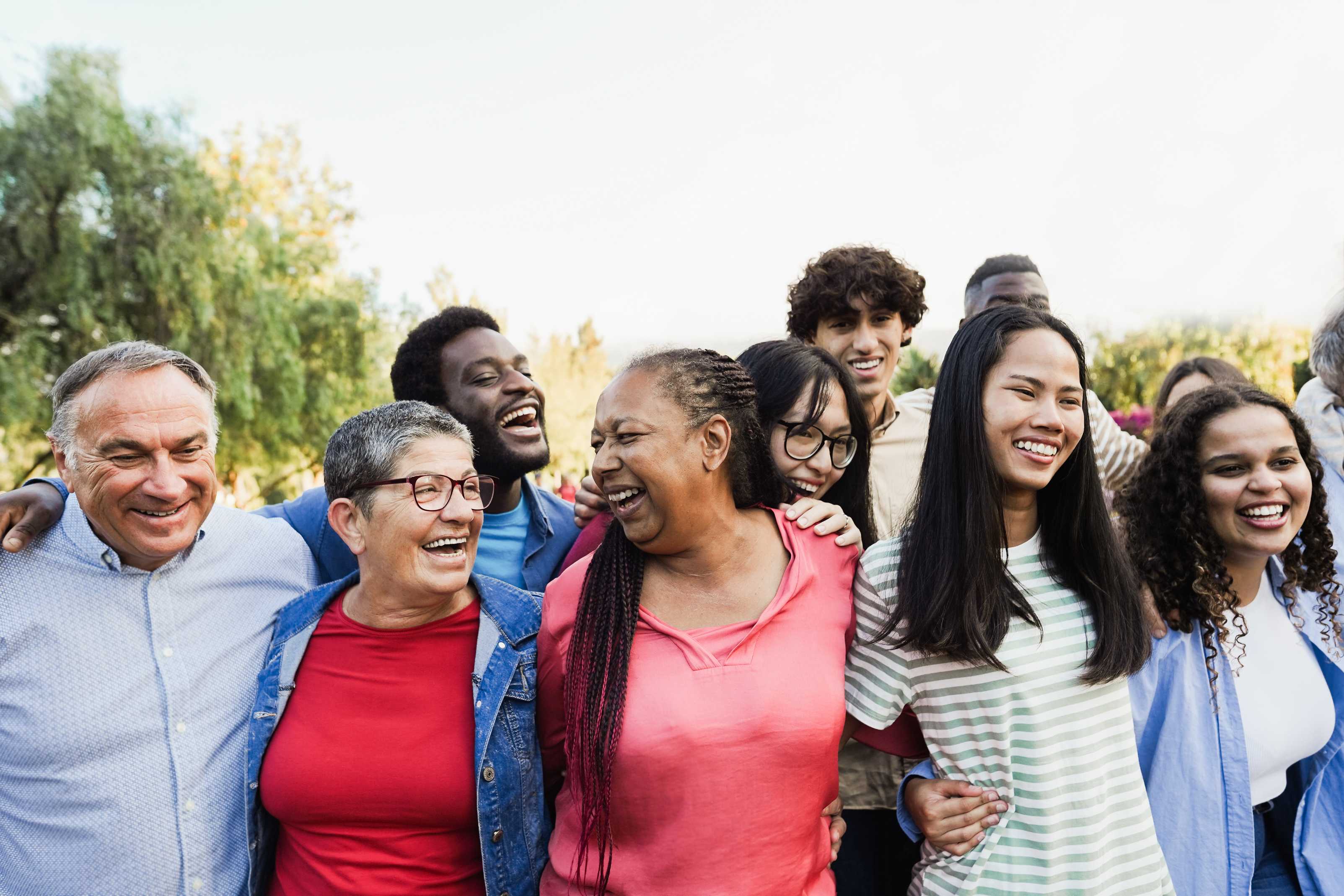 A diverse group of people pose for a photo with their arms around each other, smiling and laughing.