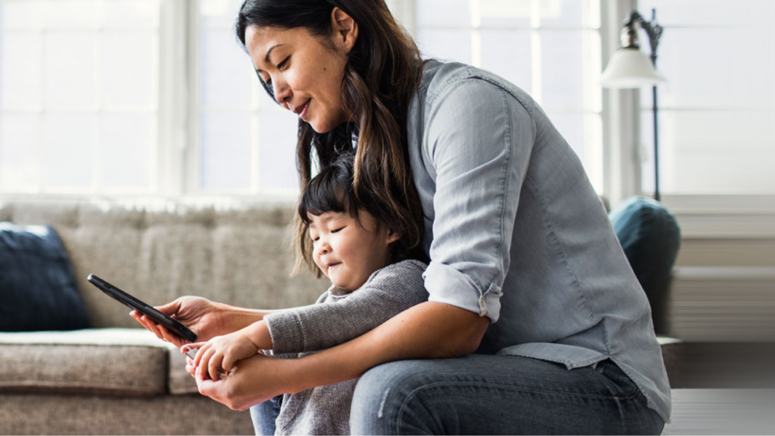 A woman and her toddler look at a smartphone in their living room.