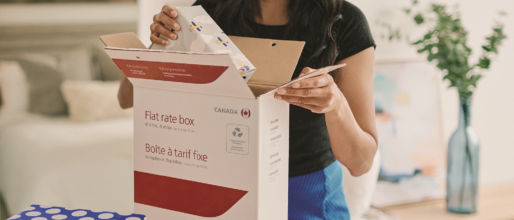 A woman packs a wrapped present into a flat rate box from Canada Post.